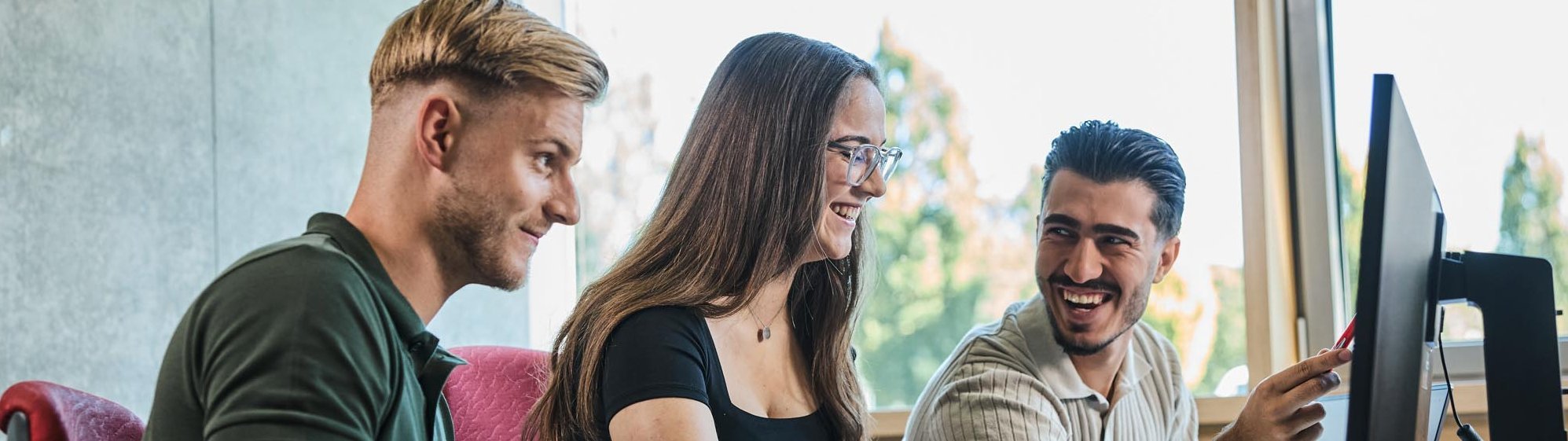 Studierende sitzen gemeinsam vor einem Computer und unterhalten sich.