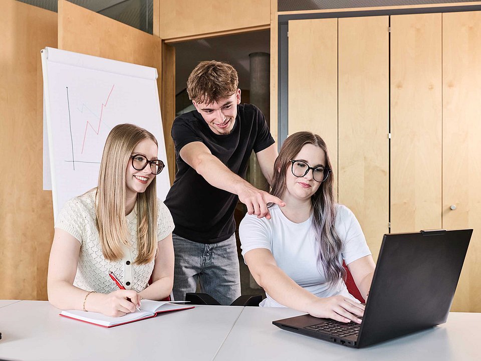 drei Azubis schauen sich gemeinsam etwas am Laptop an, während einer davon etwas erklärt