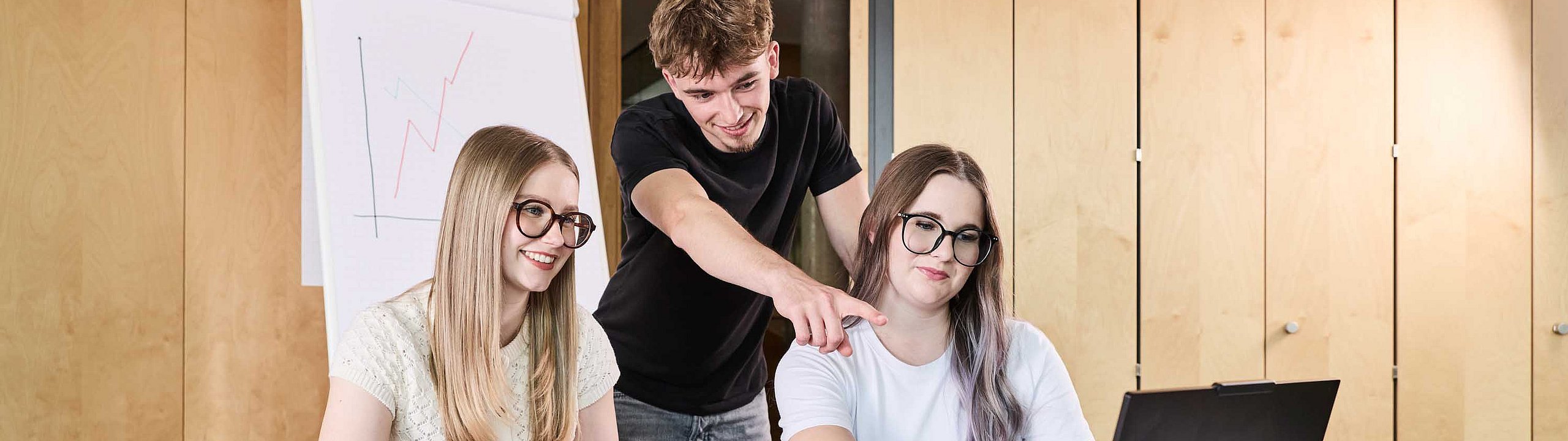 Studierende sitzen gemeinsam vor einem Computer und unterhalten sich.