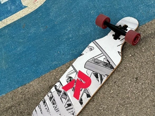 Auf einem Sportplatz liegt ein Skateboard mit den Rollen nach oben, das rote Rieker Sport Logo prangt in der Mitte der Unterseite des Skateboards.