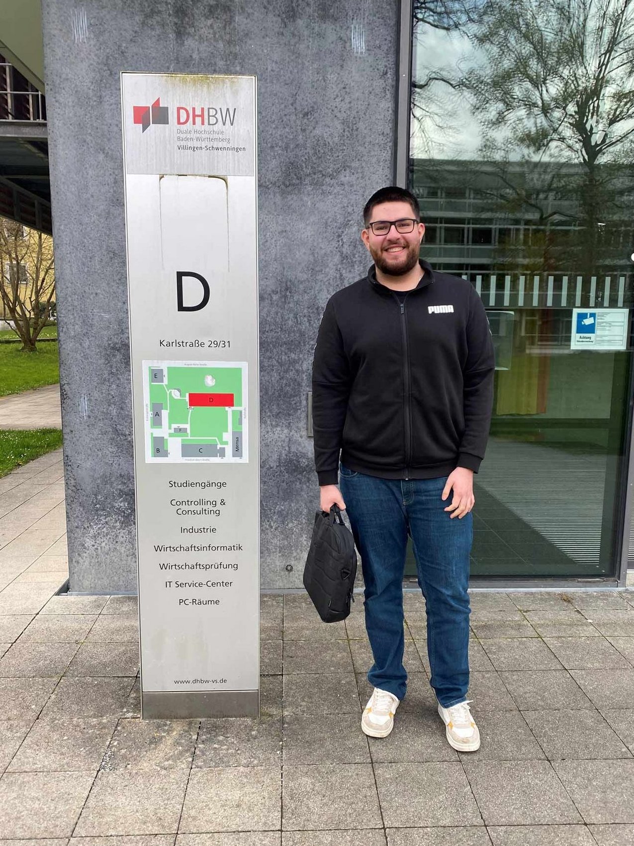 Der duale Student Alpay steht vor einem Gebäude der DHBW Villingen-Schwenningen.