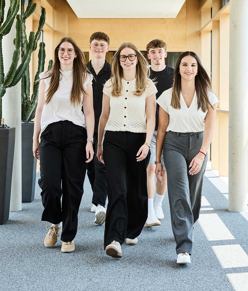 Auszubildende und Studierende von Rieker laufen einen Gang im Unternehmensgebäude entlang.