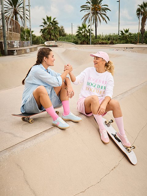 Zwei junge Frauen in trendiger Alltagskleidung und Sneakern lachen zusammen und tragen Rieker Sport Sneaker.