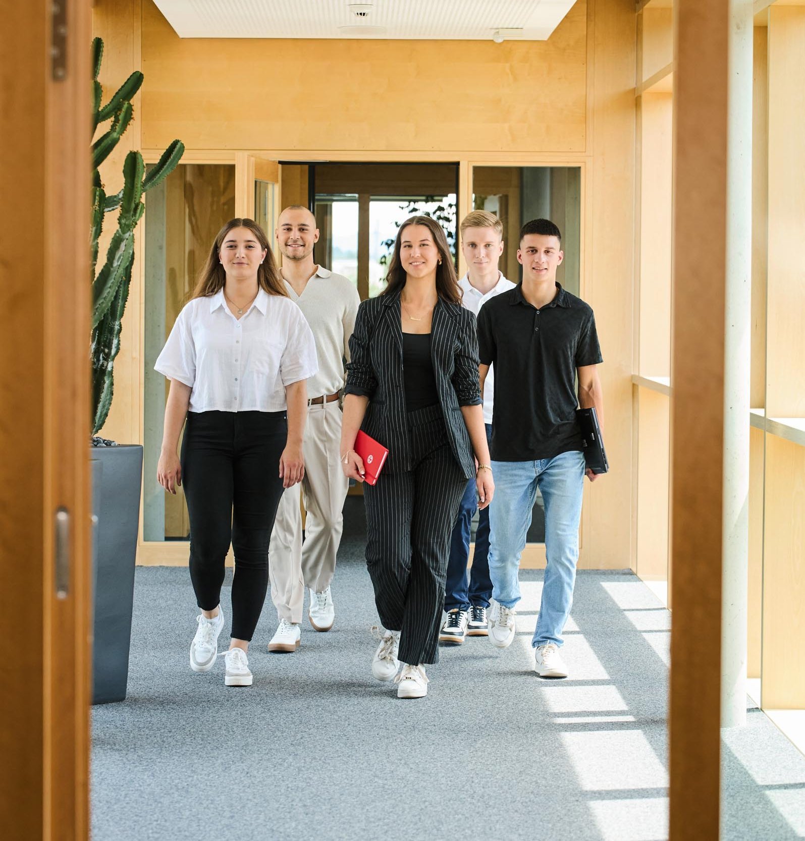 Auszubildende und Studierende von Rieker laufen einen Gang im Unternehmensgebäude entlang.