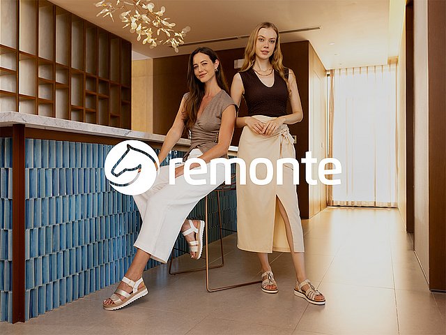 Zwei Frauen in eleganter Kleidung mit edlen Sandaletten sprechen miteinander. Mittig im Vordergrund ist das remonte Logo grafisch platziert.