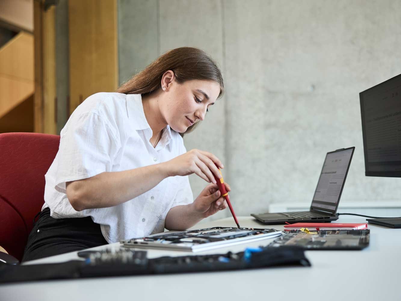 Eine Auszubildende sitzt an einem Schreibtisch und schraubt an einer Platine.