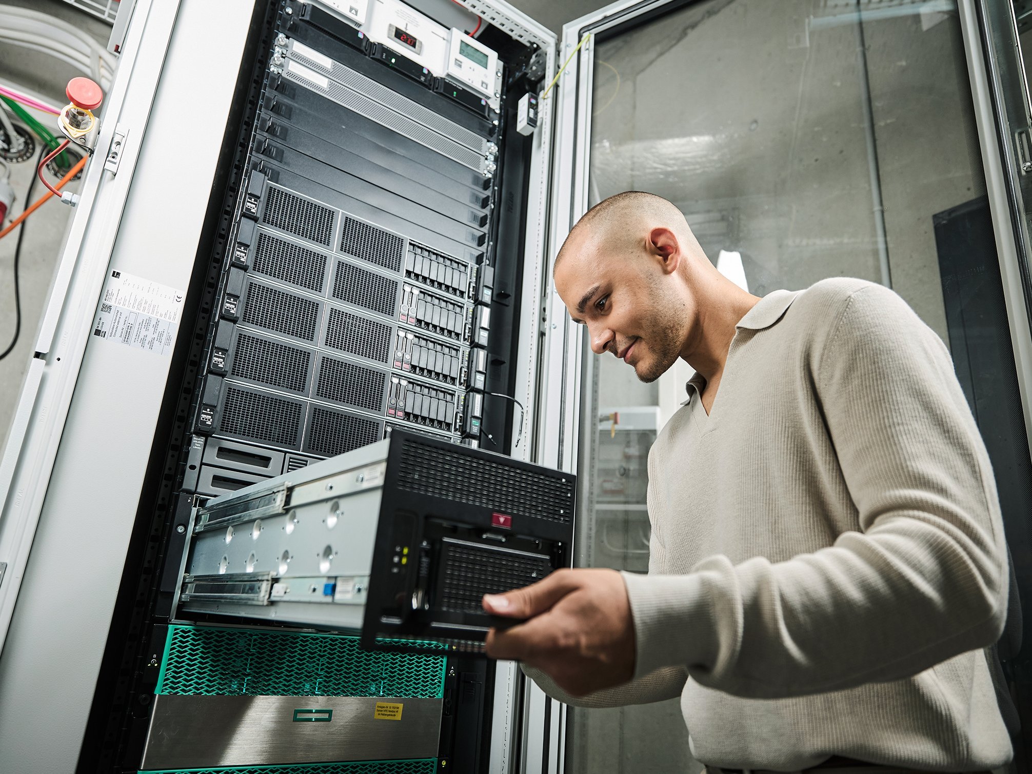 Ein Auszubildender steht vor einem Serverschrank.