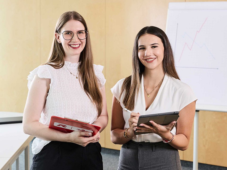 Zwei Auszubildende stehen im Büro mit ihren Unterlagen