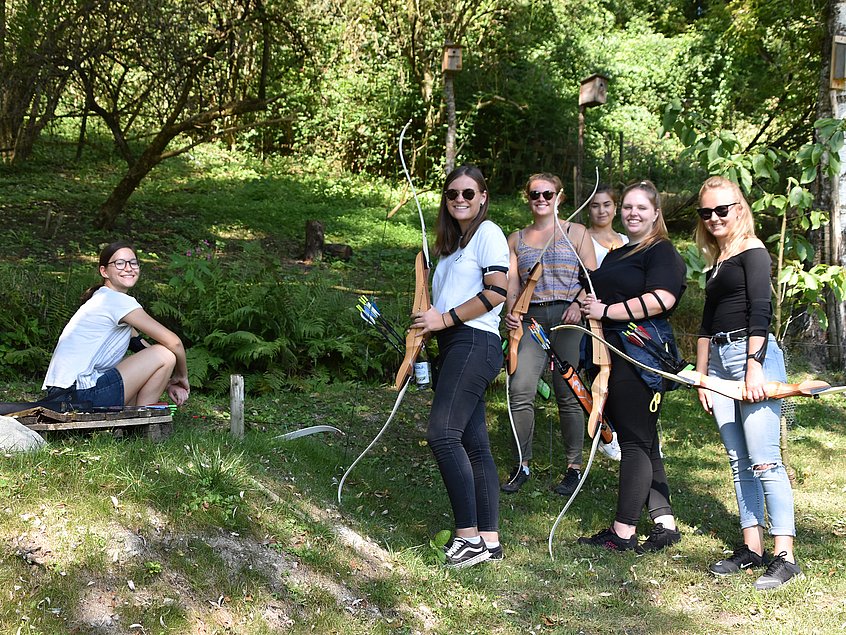 Rieker Auszubildende und dual Studierende beim Bogenschießen in einem Wald.