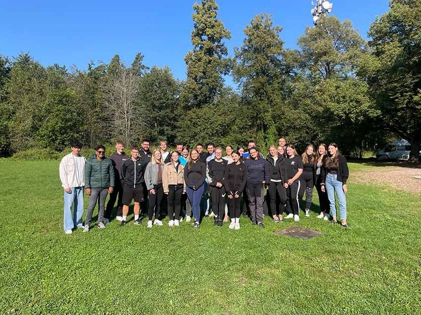 Eine Gruppe Auszubildender und Studierender von Rieker posieren für ein Gruppenfoto auf einer Wiese bei Sonnenschein.